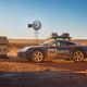 A 2023 Porsche 911 Dakar is parked in front of a windmill and a gas pump.